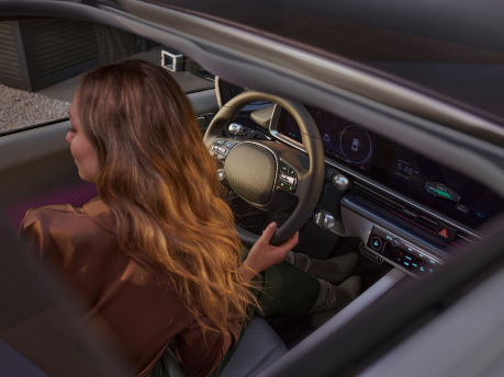 woman inside the Hyundai IONIQ 6 with one hand on the steering wheel putting on the seat belt